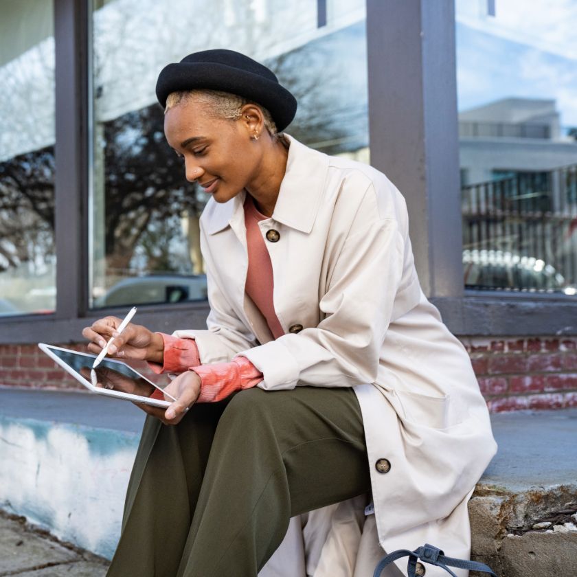 A person works on a digital design on their tablet while sitting outside a building.