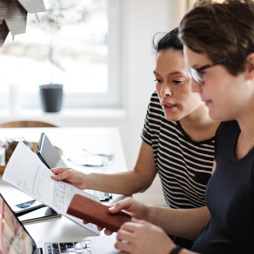 Two people sat at their kitchen table look at their laptops and an invoice while reviewing their household budget.