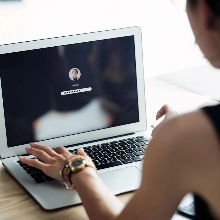 Person enters a password on a laptop login screen, focusing on secure access management.
