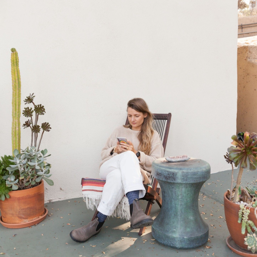 Person sitting outdoors in a chair surrounded by potted plants, using a smartphone, representing a moment of relaxation.