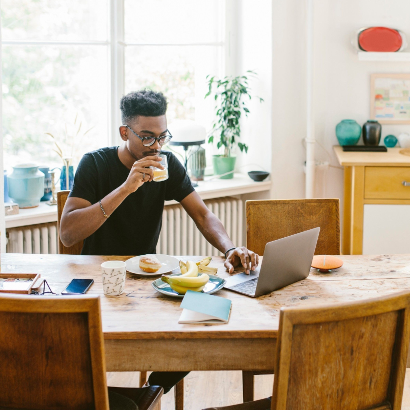 A person sits at their kitchen table, eating breakfast and drinking juice as they back up files on their laptop.