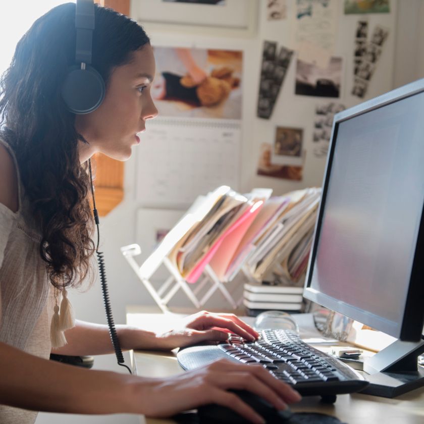 A freelance translator wears headphones to listen to some audio while looking at their computer screen.