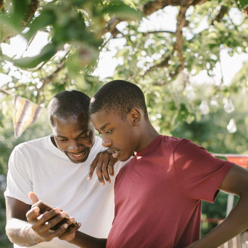 Two people stood under a tree look at a mobile device, discussing how to maintain the quality of a video they are sending.