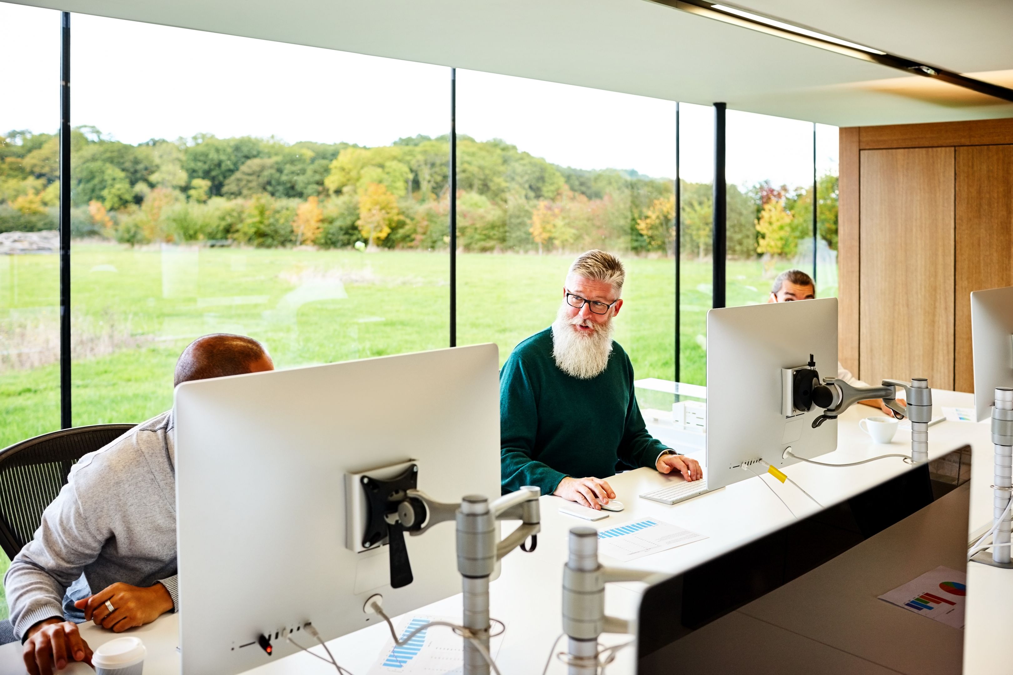 Office workspace with employees using Macs, discussing signing PDFs.