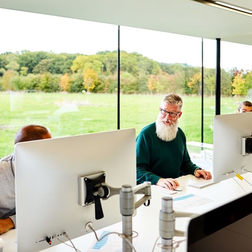 Office workspace with employees using Macs, discussing signing PDFs.