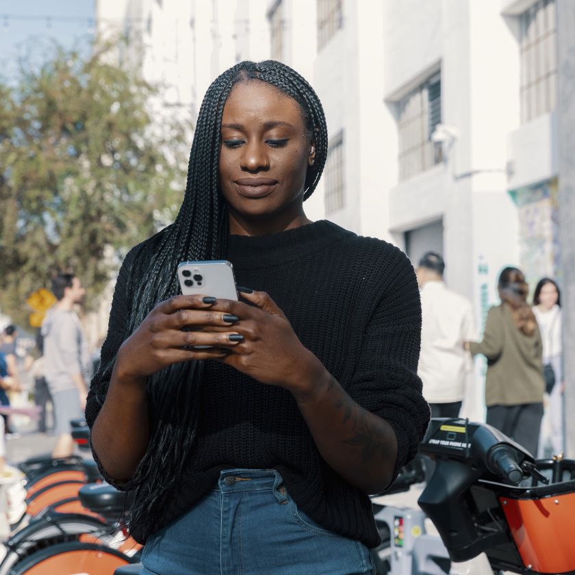 Person walking down a street lined with trees and buildings while looking at their smartphone.