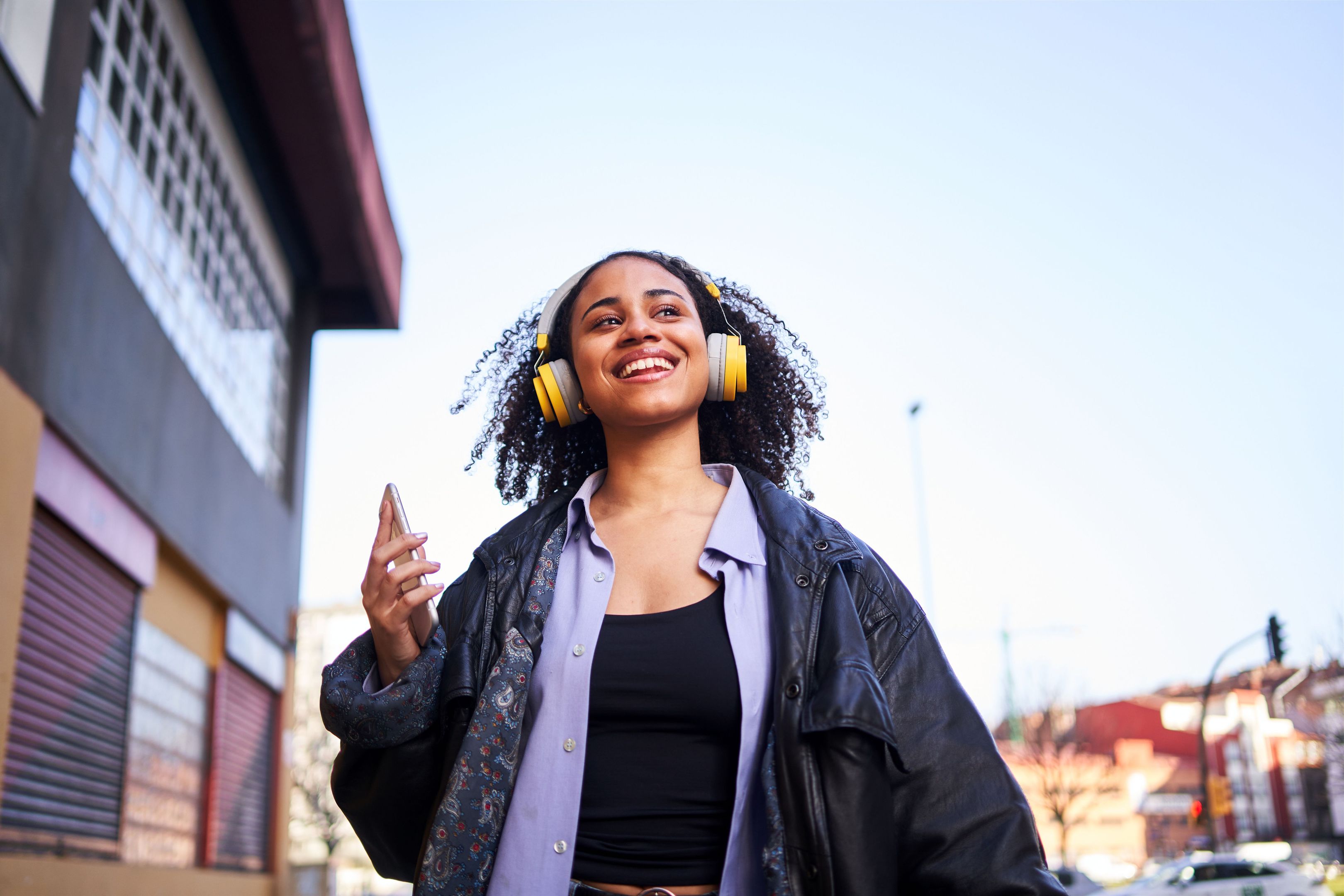 A person with headphones on walks down a street holding their mobile device, listening to music that hasn't been compressed.