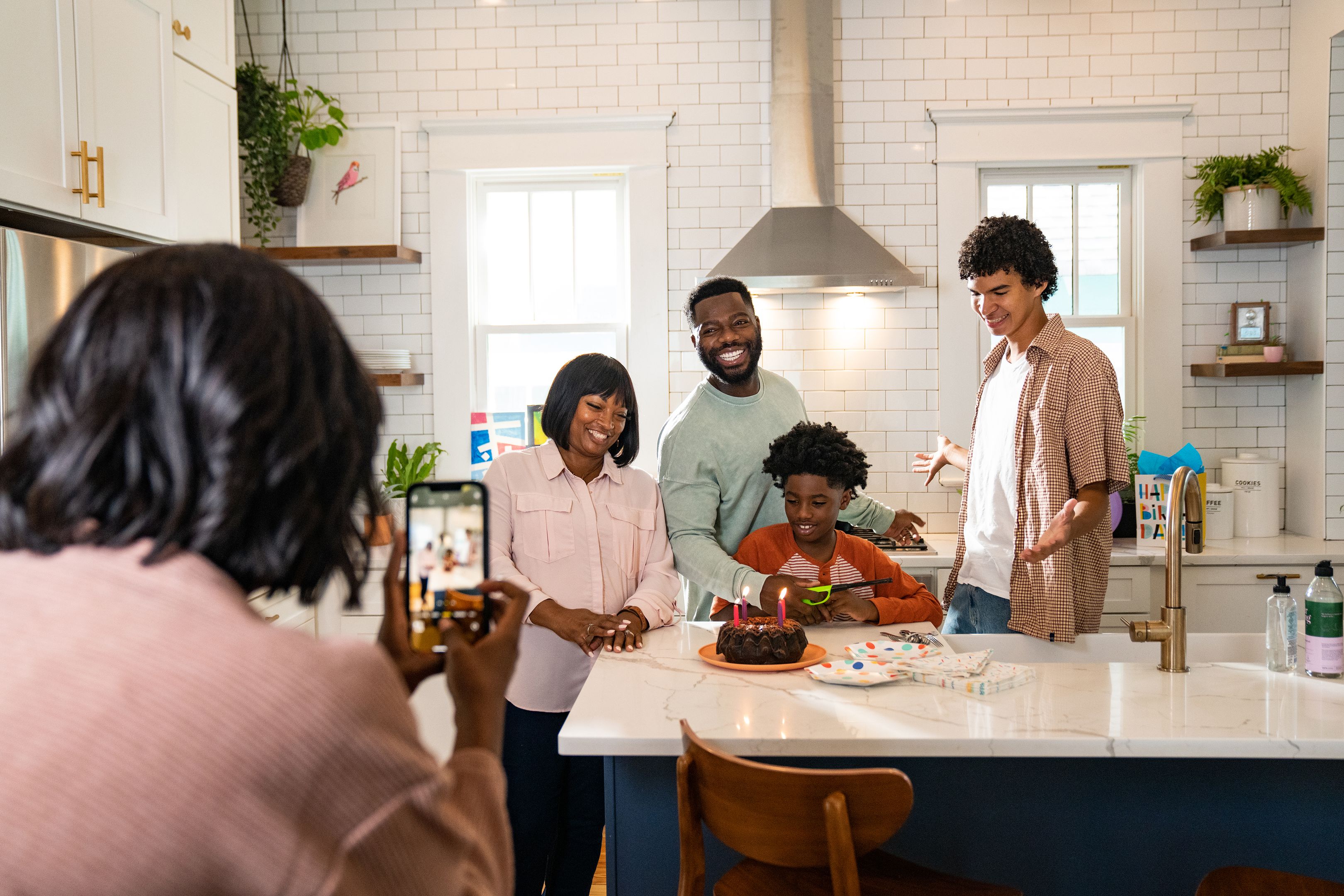 Using a mobile device, someone takes a photo of a family standing around a child and their birthday cake.