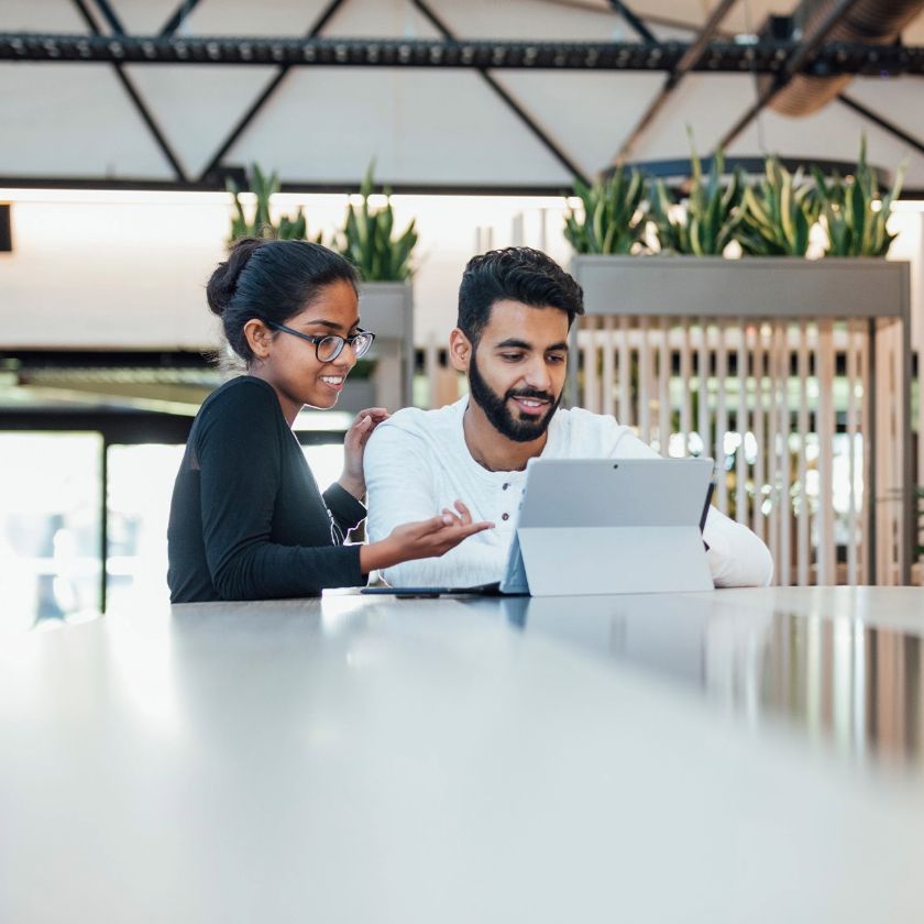 Two people work in an office and look at a tablet together while working on a marketing campaign.