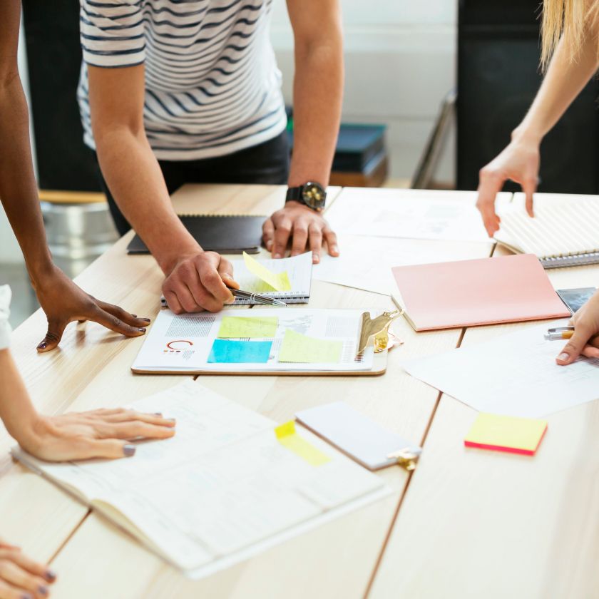 A group of people huddle around a notepad at an office table while brainstorming.