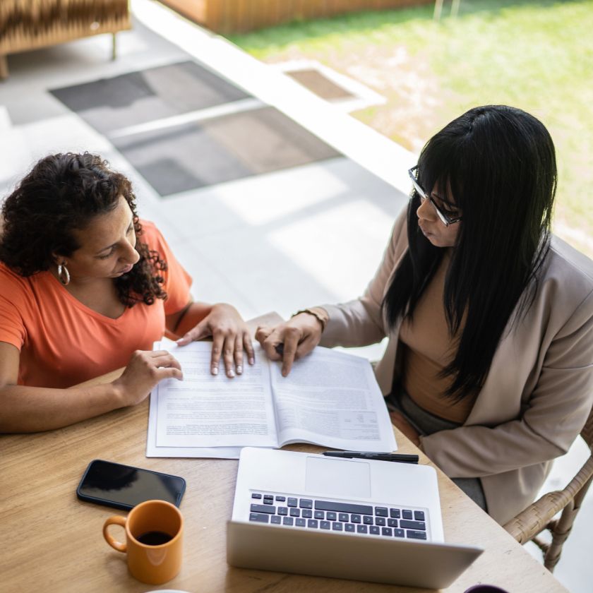 A legal professional looks over a document with two other people while they sit at a dining room table.