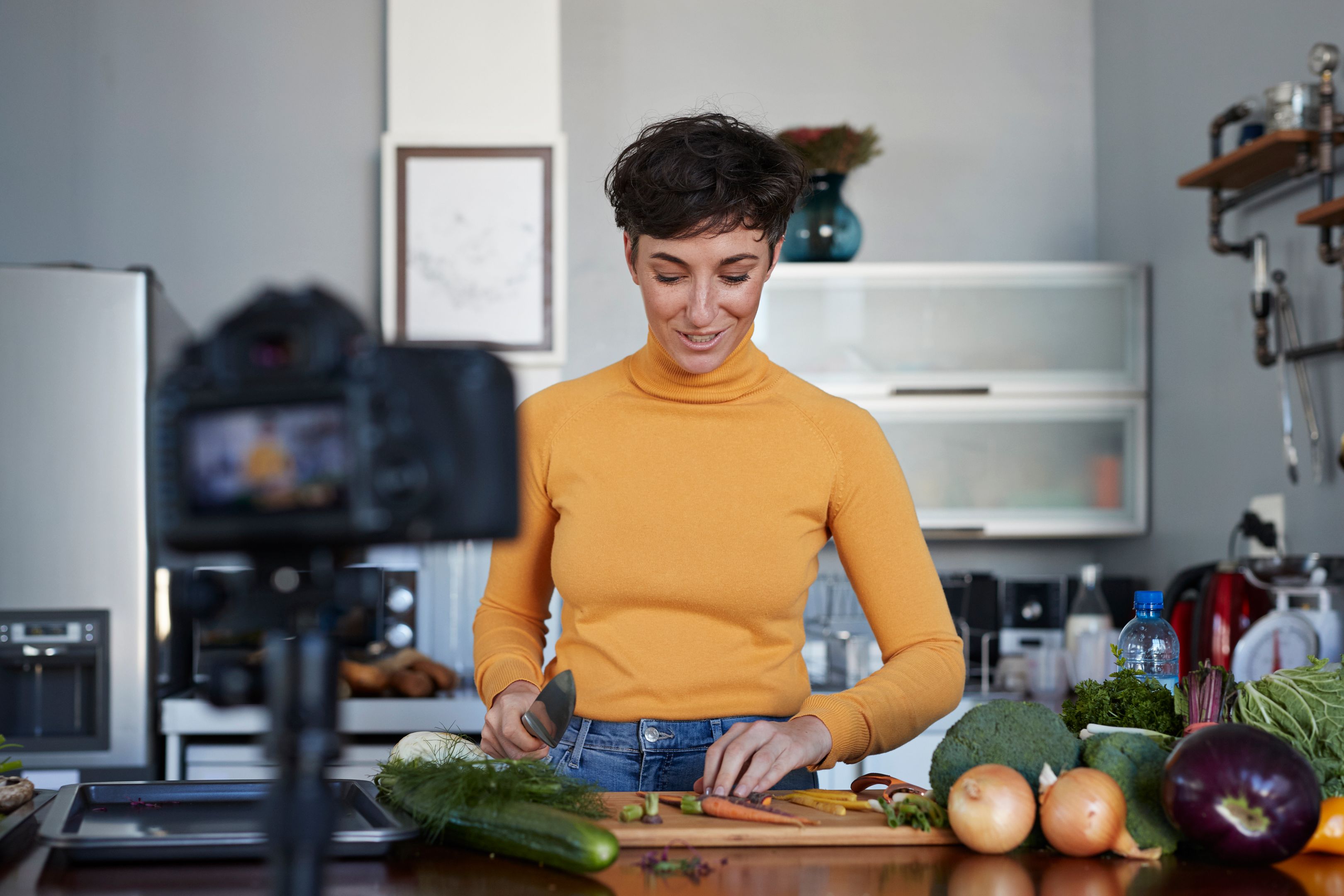 A vlogger films themselves prepping vegetables in their kitchen.