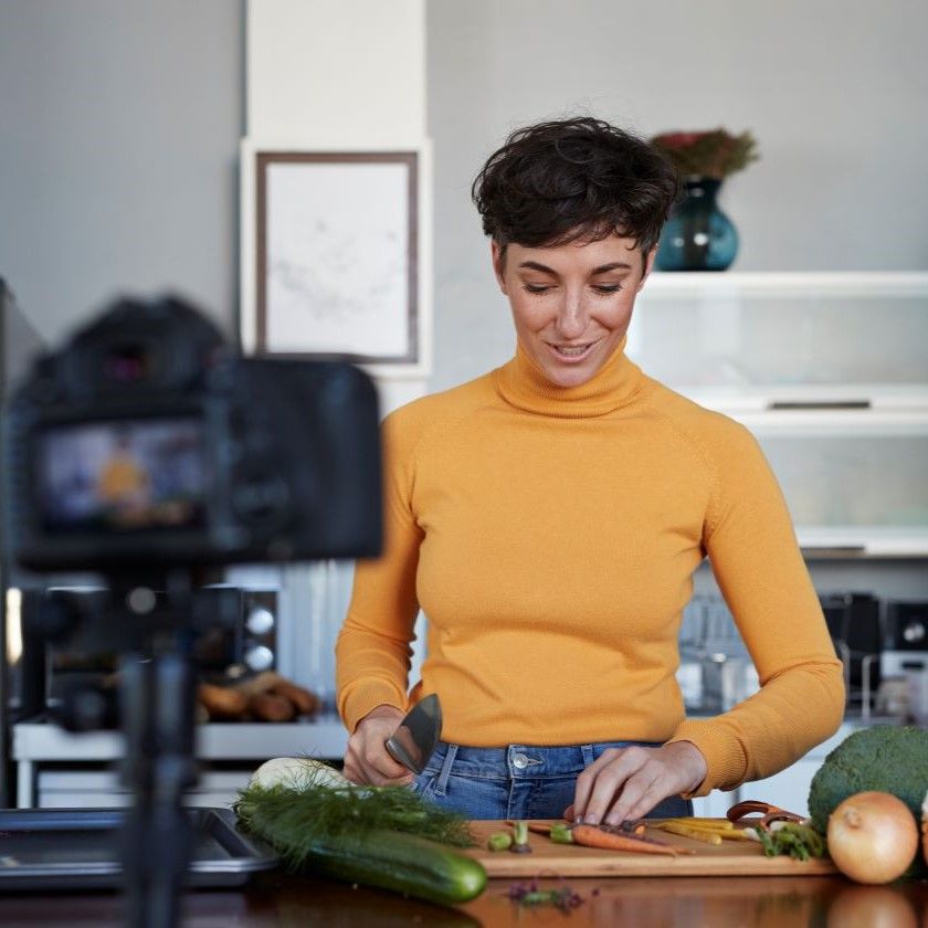 A vlogger films themselves prepping vegetables in their kitchen.