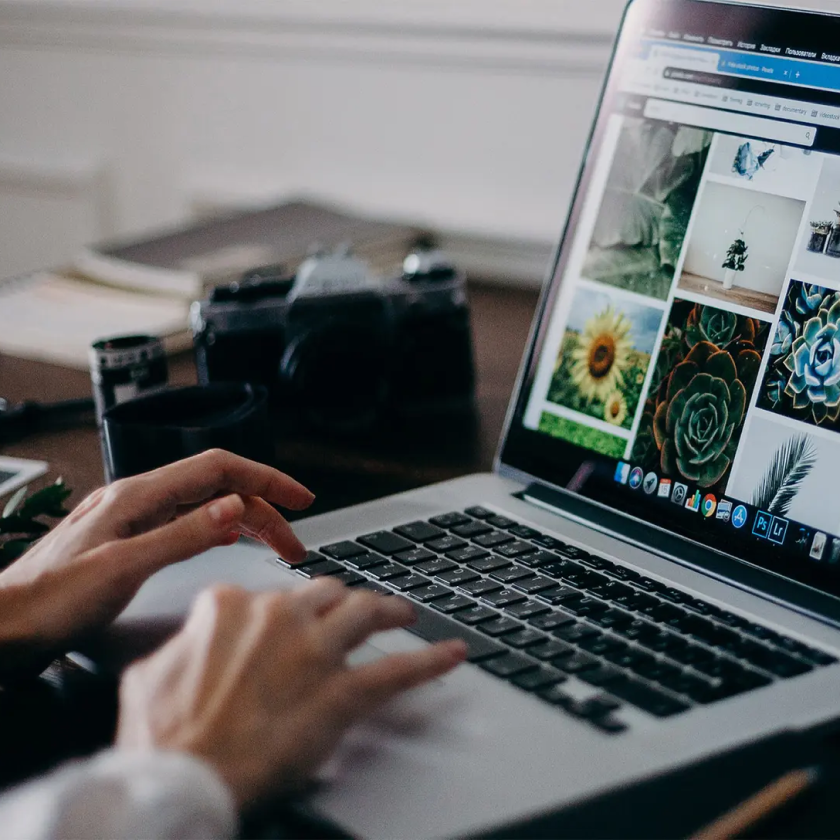 A person uses their laptop to browse and organize their photos, a camera on the desk beside them.