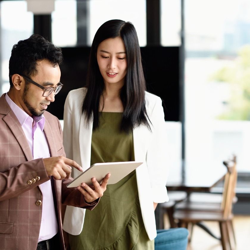 Two people share notes on a tablet device while collaborating in their office during the marketing approval process.