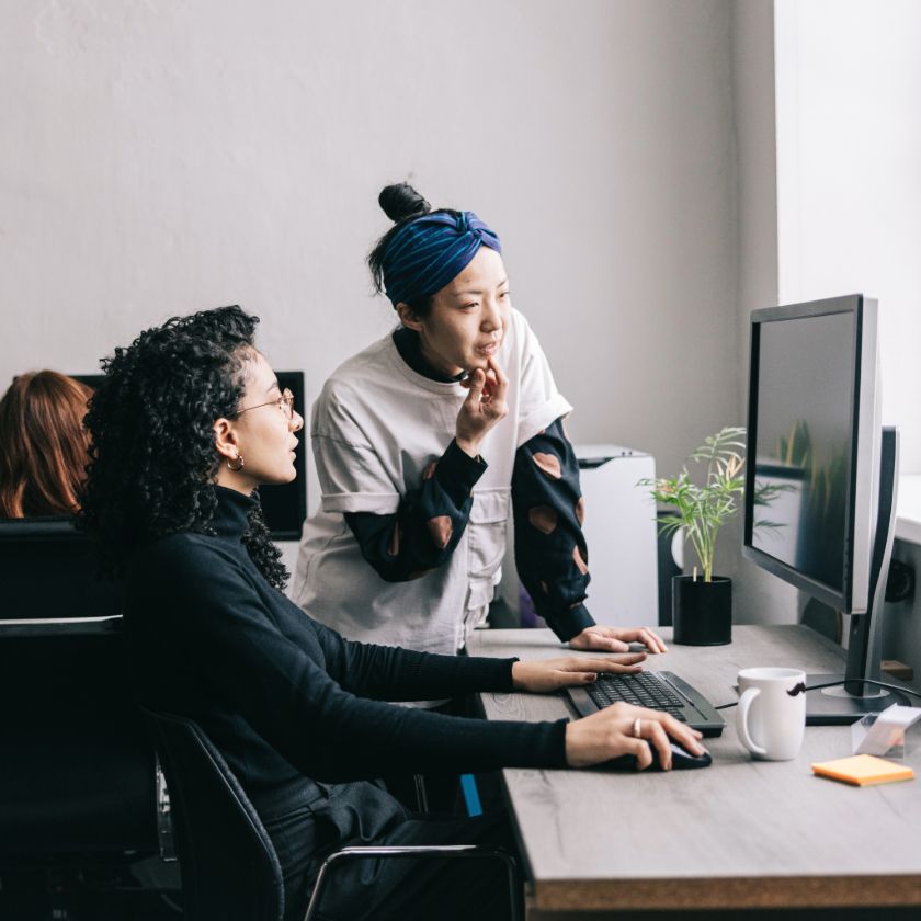 Two people in an office look at a computer screen together, discussing edits to make to a file.