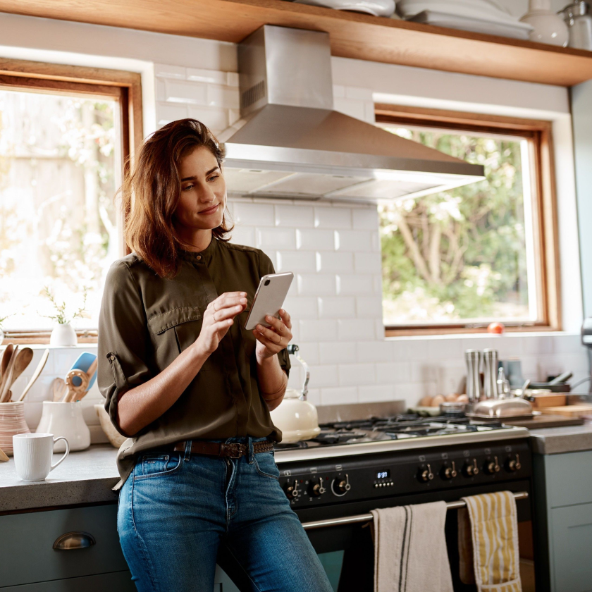 A person leans back against their kitchen counter, smiling as they send a large file using their mobile device.