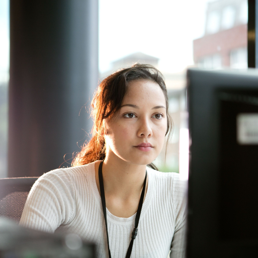 Person focused on a computer screen in an office setting, appearing engaged in work or research tasks.