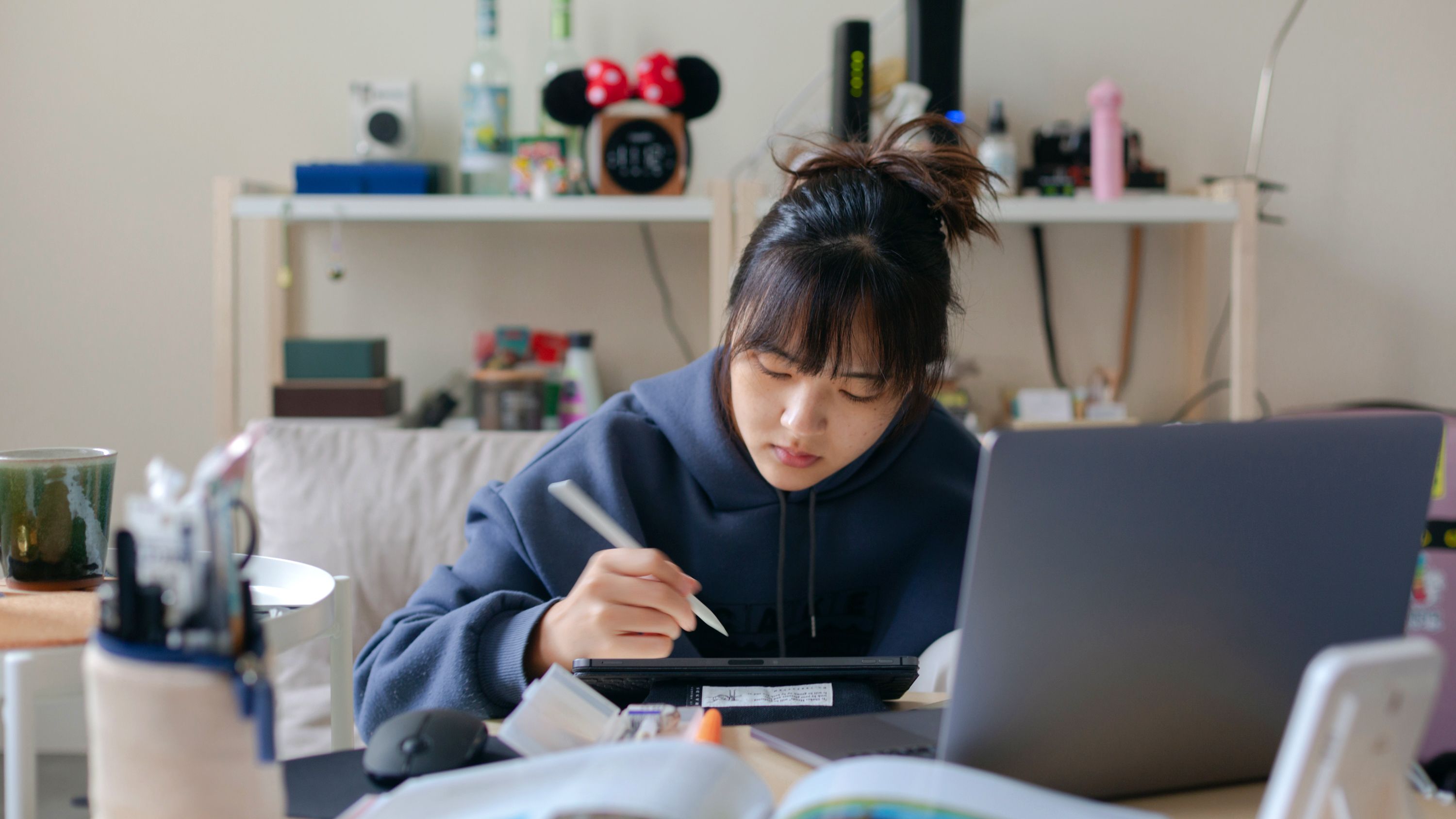 Person sketches on a tablet while working at a desk with a laptop, representing digital creativity and remote work.