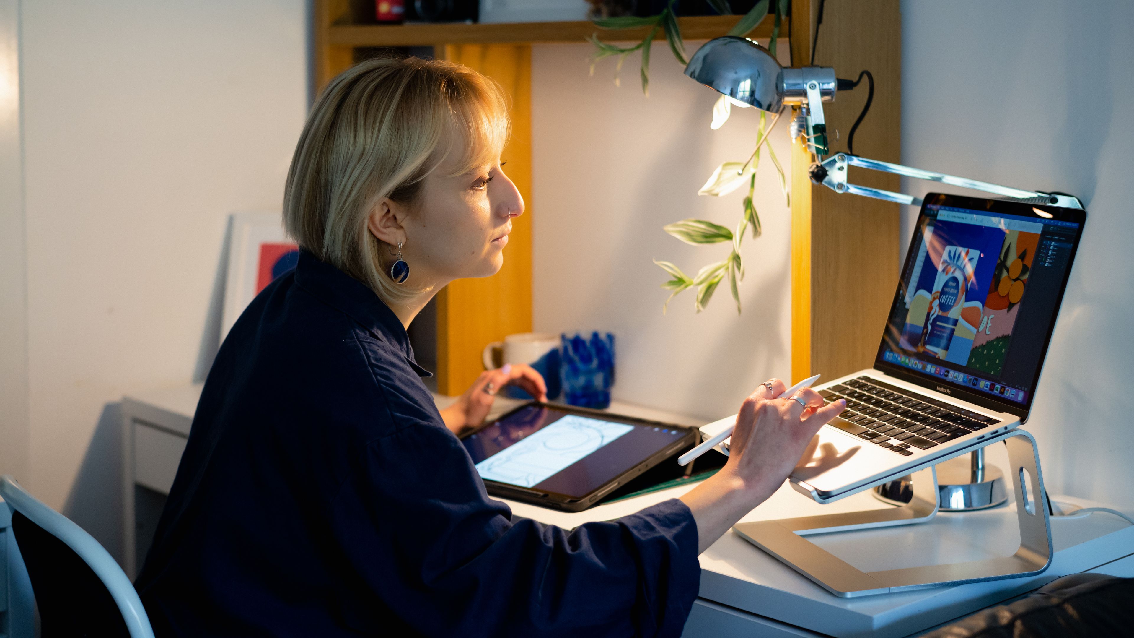 A person creates digital artwork on a tablet while using a laptop as a reference.