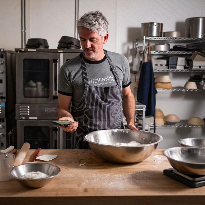 A person checks their phone while preparing food in a commercial kitchen.