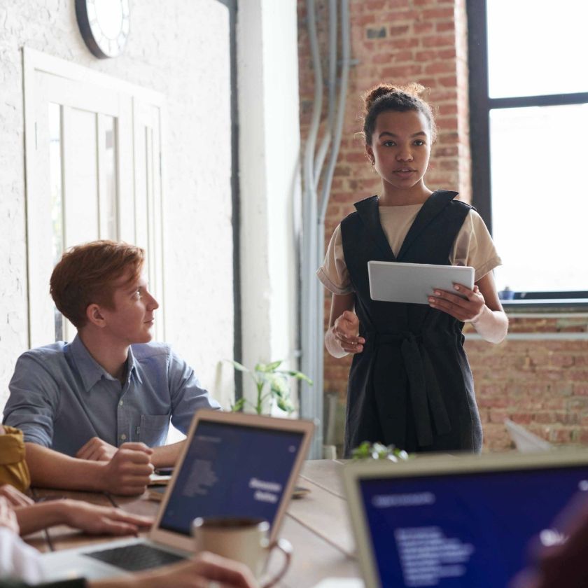 A team sits around a desk and faces someone who delegates tasks to them.