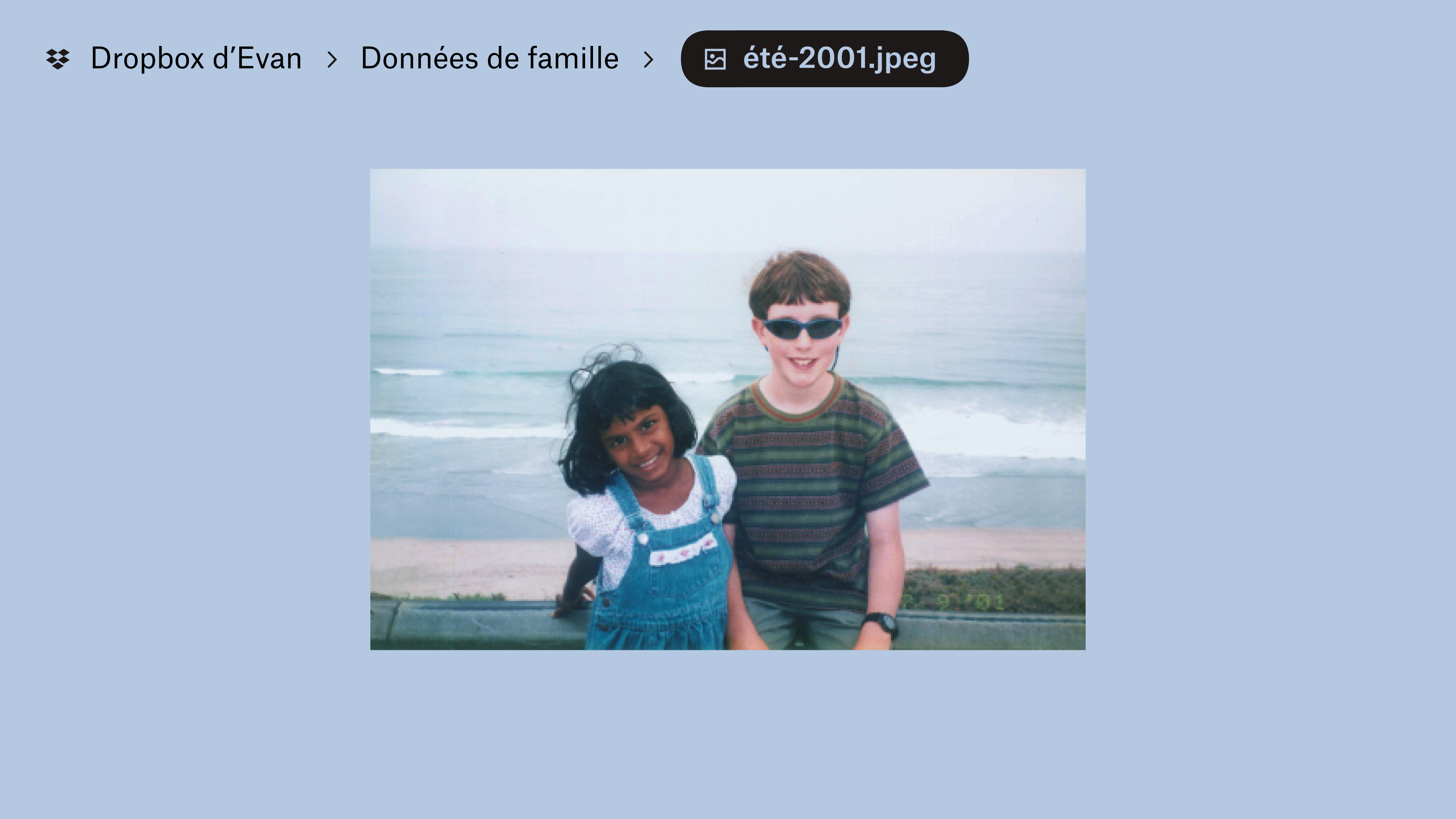Une photo stockée dans le dossier « Documents familiaux » du Dropbox d’Evan. Deux jeunes enfants sourient devant l’objectif, avec en arrière-plan des vagues sur une plage.