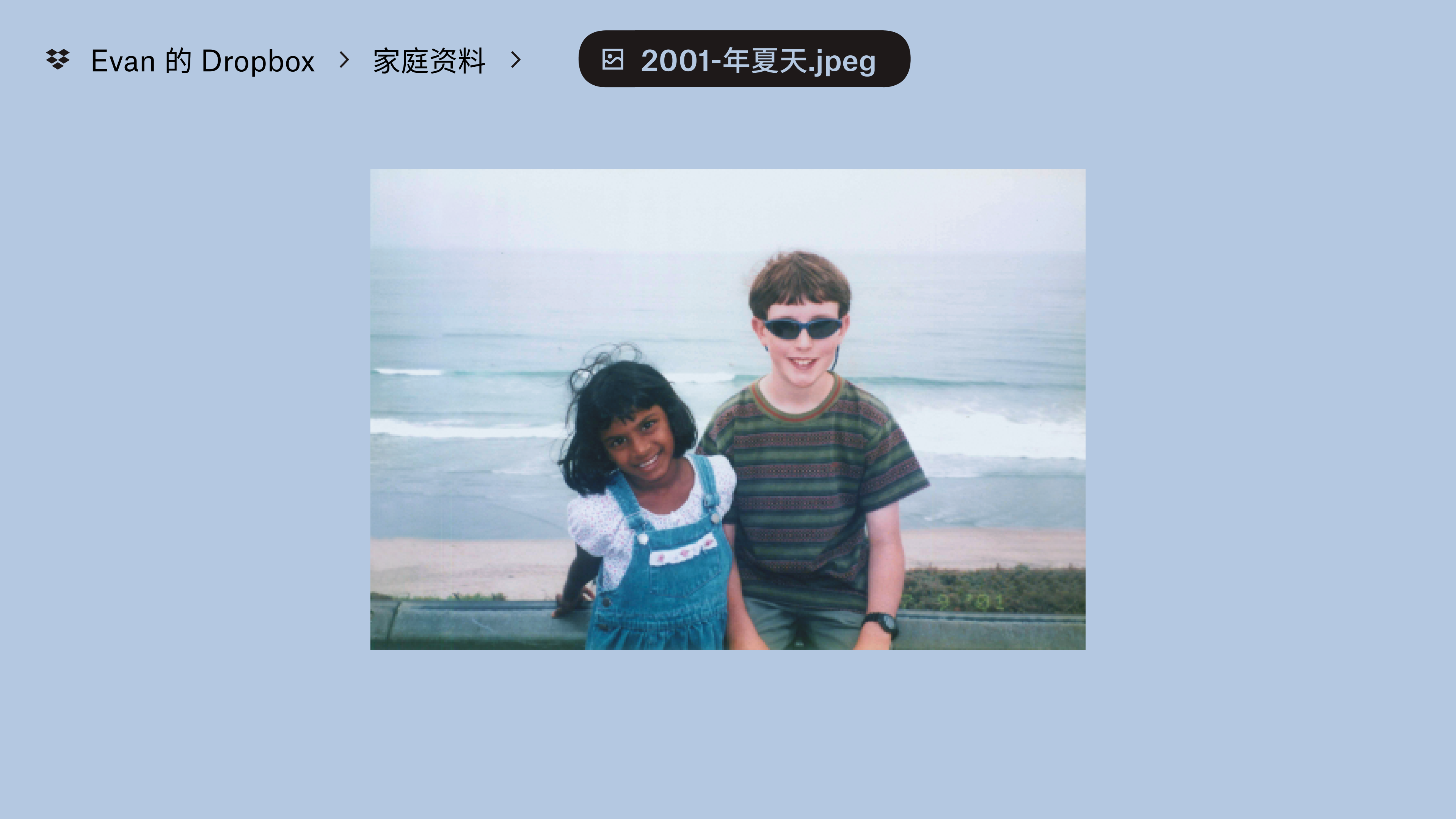 一张存储在“Evan's Dropbox”的“Family Stuff”文件夹中的照片。两个孩子对着镜头微笑和挥手，身后是一片海滩。