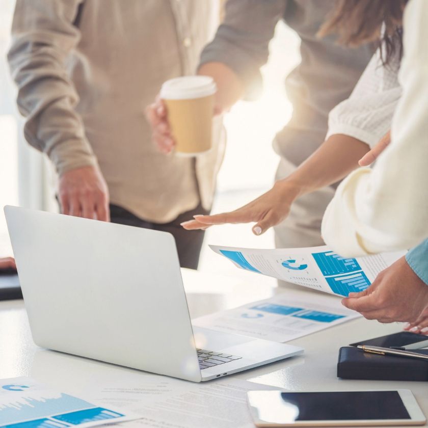 A sales team stands around a table with a laptop and sales materials.