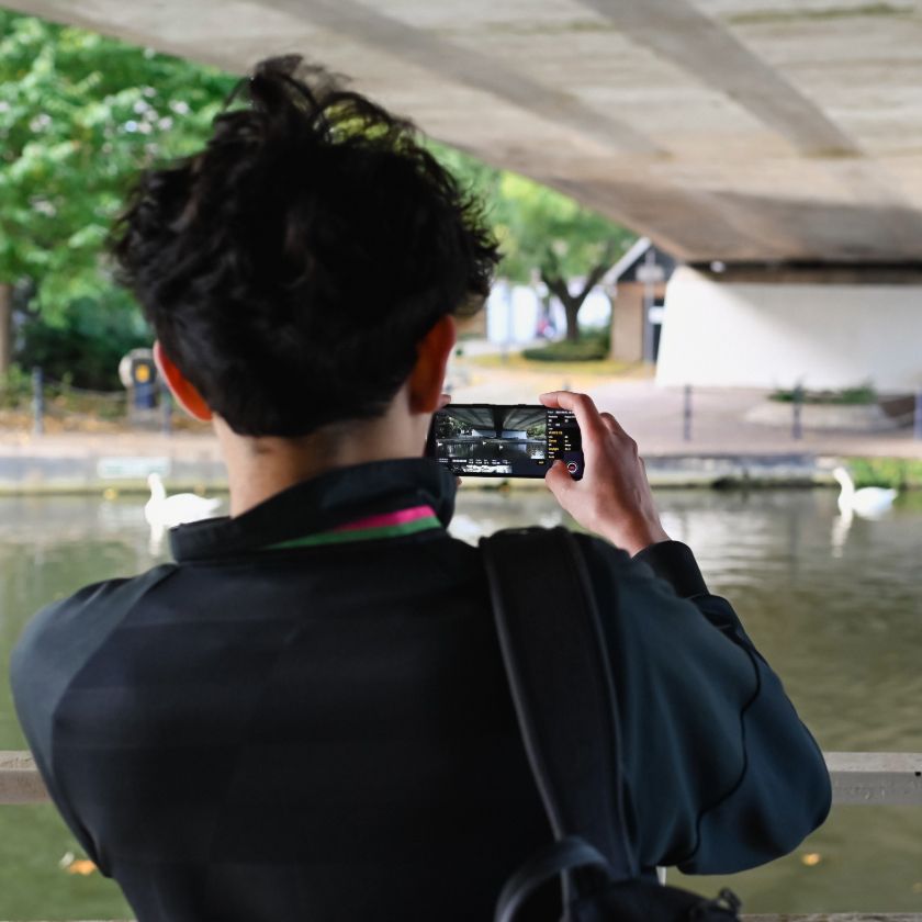 A beginner videographer captures footage of swans swimming in a river beneath a bridge.