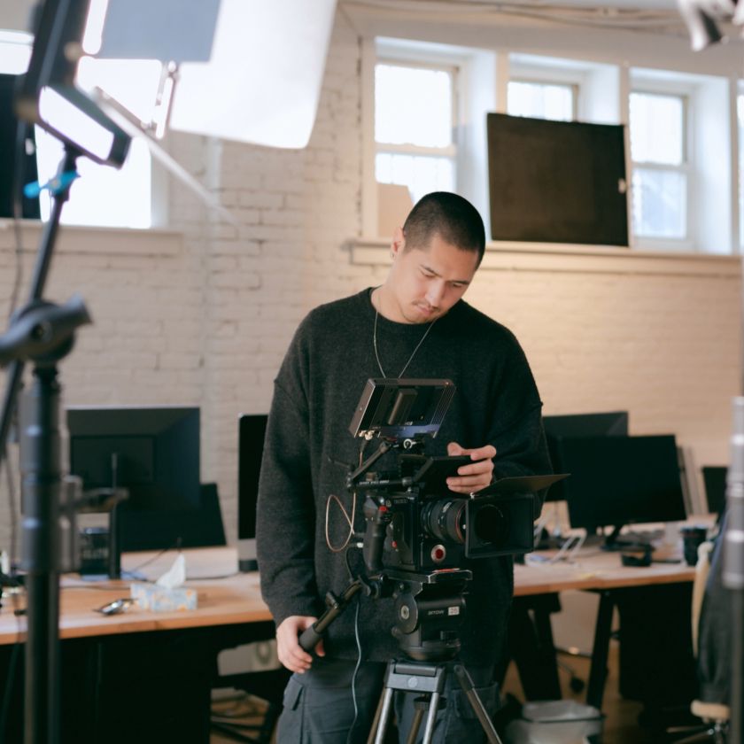A videographer holds their camera and looks at their footage on the camera monitor.