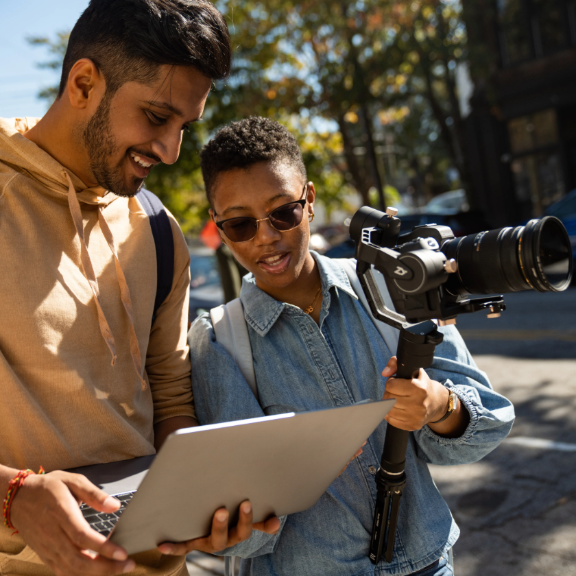 A videographer and crew member consulting their laptop while filming on location.