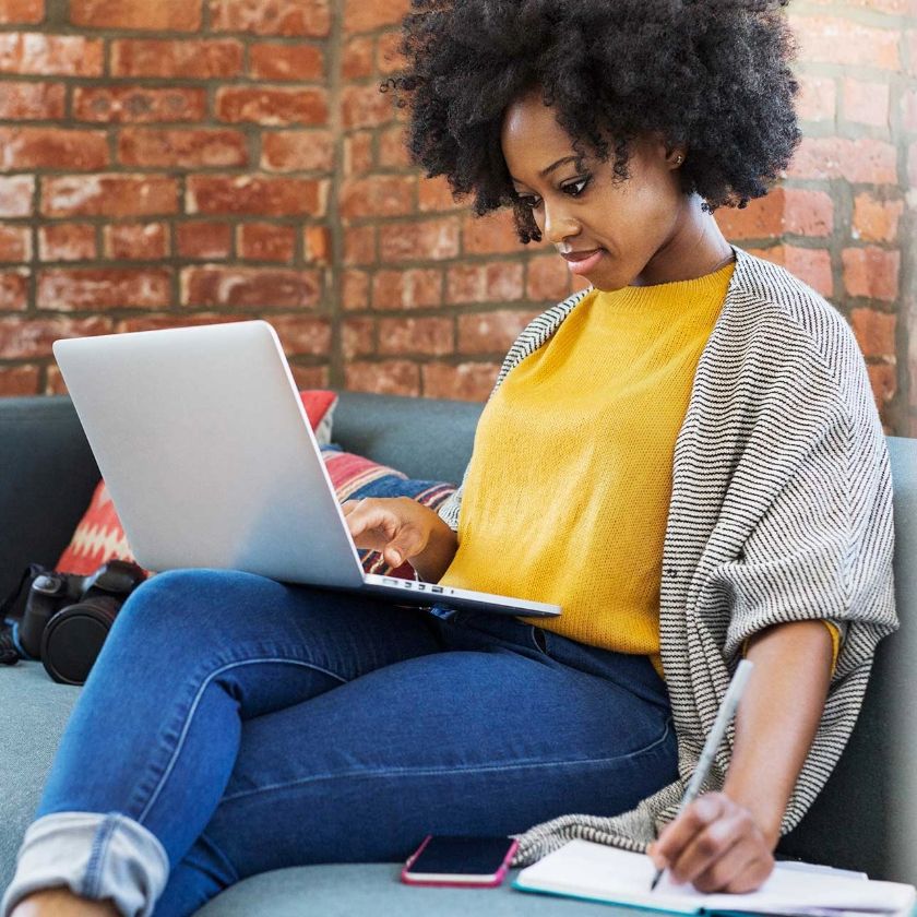 A solopreneur running their photography business from home, with a laptop on their lap as they sit on a couch.