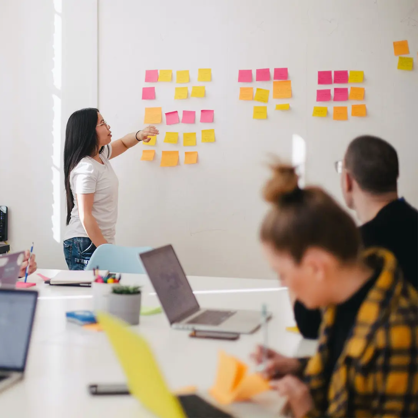 Team in a meeting setting OKRs, with one member leading a discussion using colorful sticky notes on a whiteboard.