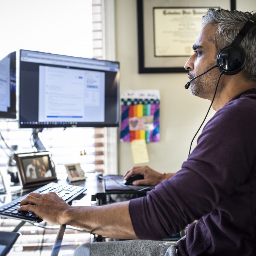 A man works in collaboration with colleagues from his home desk setup.