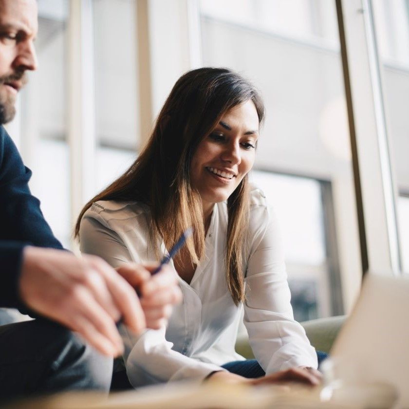 Two people collaborating on laptop at office, one holding a pen, the other reviewing PDF files onscreen.