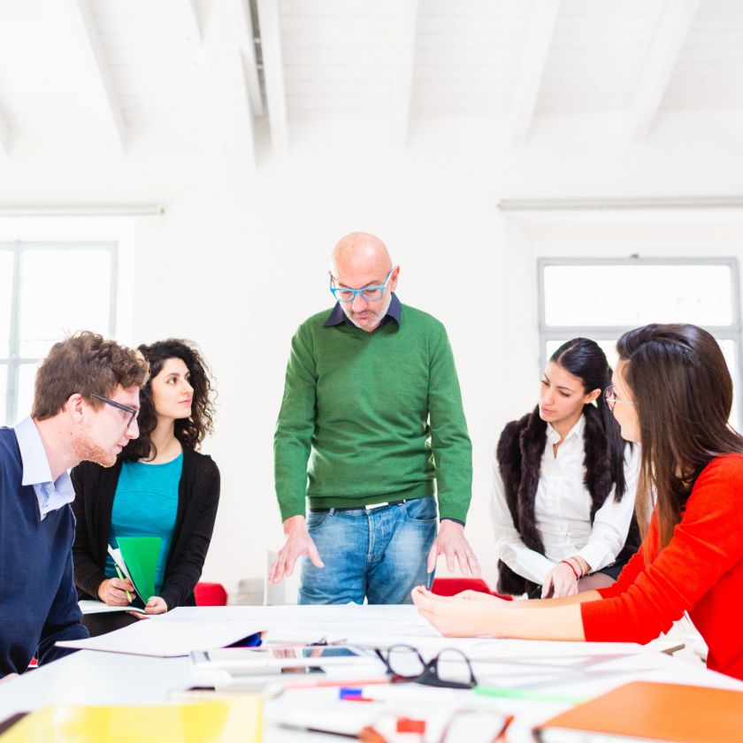 A team of people sit and stand around a desk, discussing how to set up a DMAIC process to support their project.