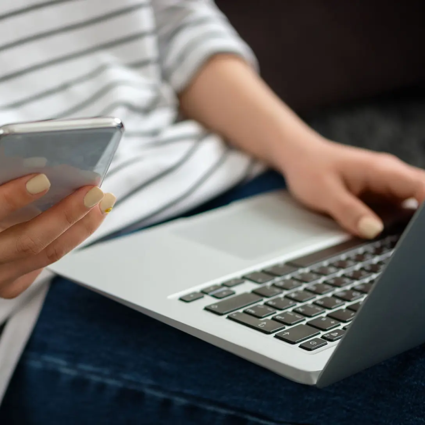 A person with a laptop on their laptop uses a mobile device to complete two-factor authentication.