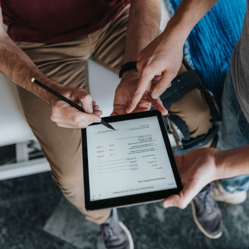 One person holds a tablet device displaying a document, while another holds a stylus pen to add an eSignature to the doc.
