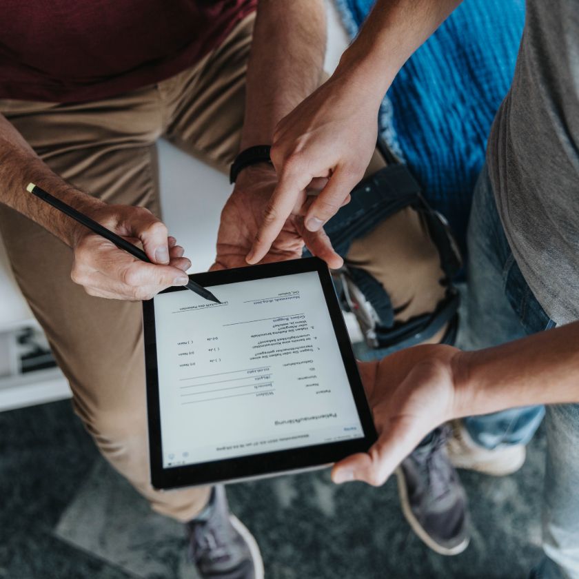 A person uses a stylus to sign a PDF on a tablet as a salesperson points to where they need to sign.