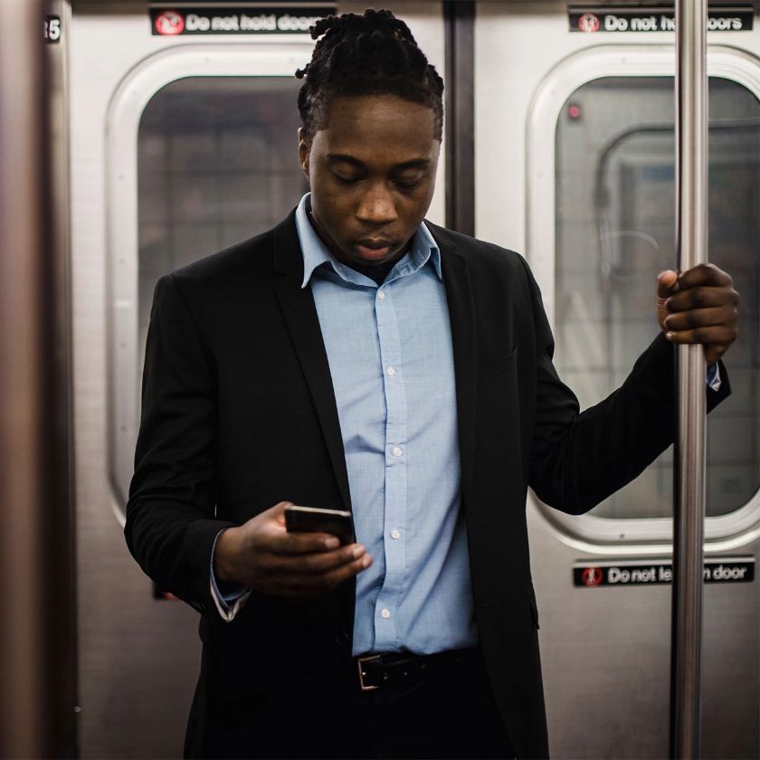 A person in a suit stands on the subway, looking at their mobile device as they try to organize their work-life balance.
