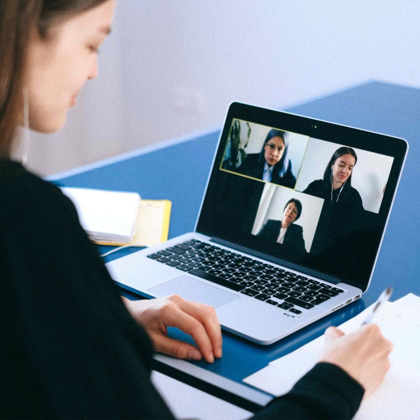 Someone sits at a desk, attending a video call on a laptop with two other participants.