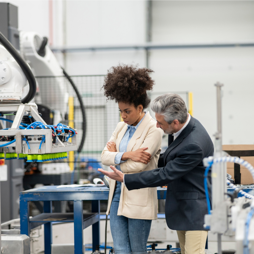Um homem e uma mulher em uma fábrica ao lado de uma máquina